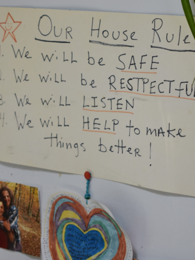 Photo of handwritten sign in family's home that reads: "Our house rules: 1) We will be safe. 2) We will be respectful. 3) We will listen. 4) We will help to make things better!