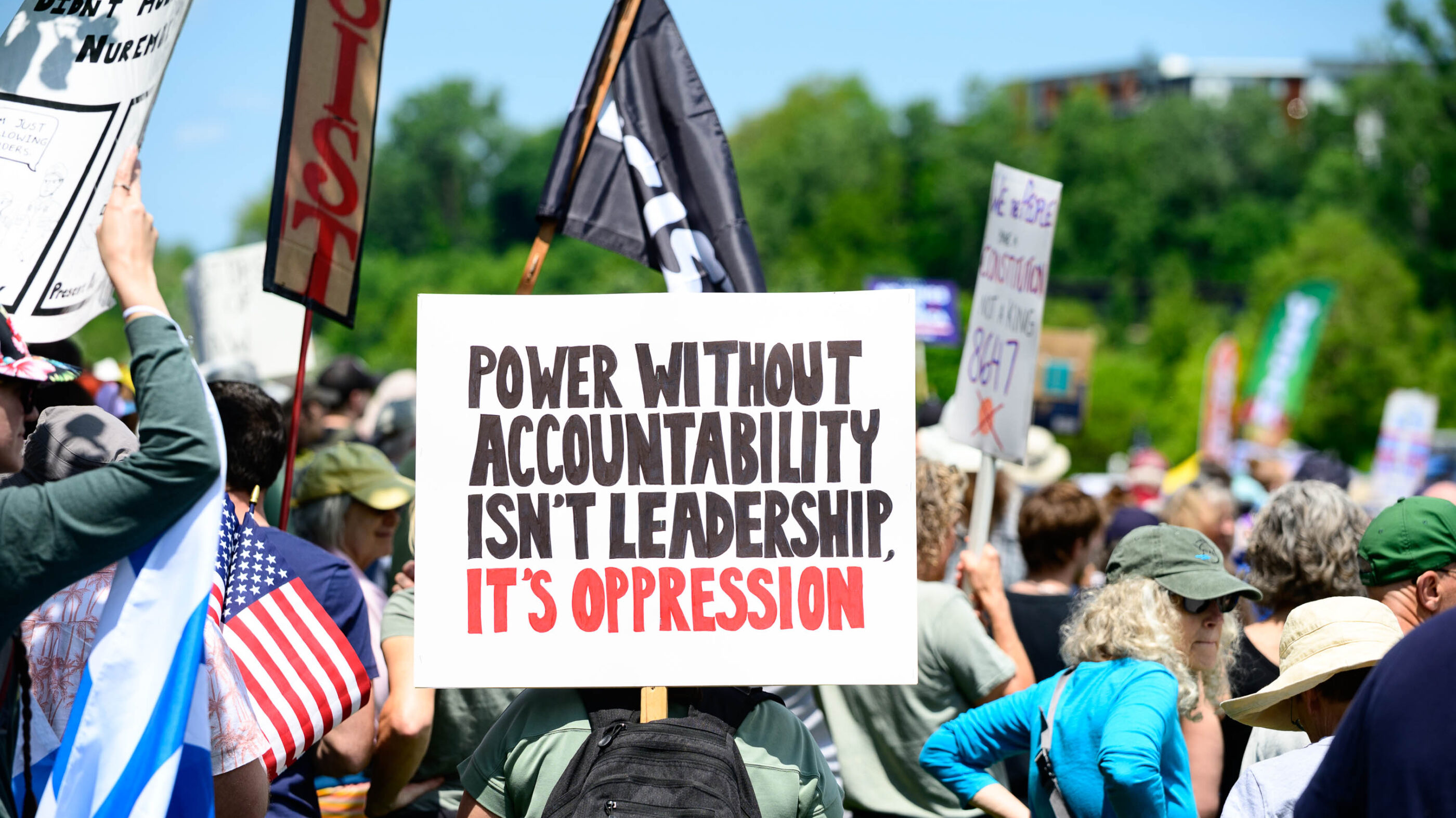 Rally crowd from No Kings Day protest, sign reads "Power without accountability isn't leadership, it's oppression"