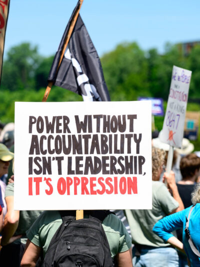 Rally crowd from No Kings Day protest, sign reads "Power without accountability isn't leadership, it's oppression"