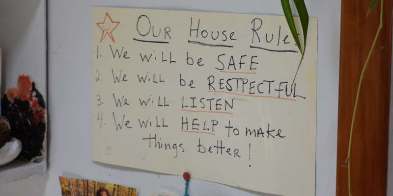 Photo of handwritten sign in family's home that reads: "Our house rules: 1) We will be safe. 2) We will be respectful. 3) We will listen. 4) We will help to make things better!