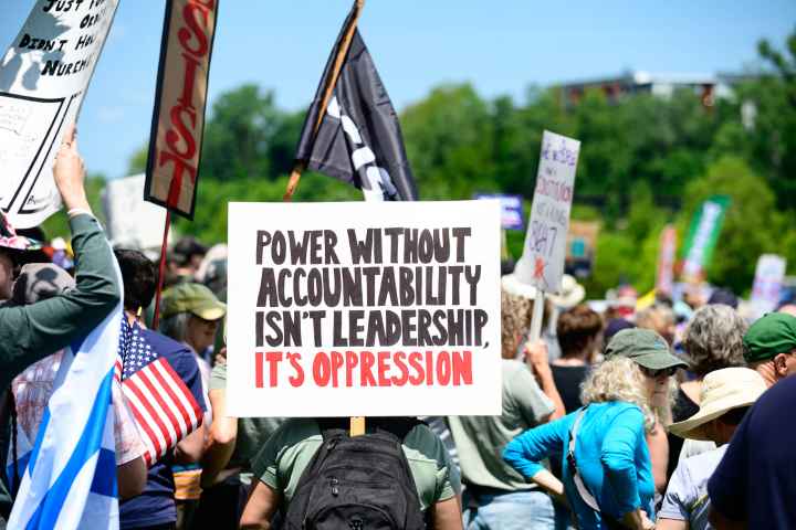 Rally crowd from No Kings Day protest, sign reads "Power without accountability isn't leadership, it's oppression"